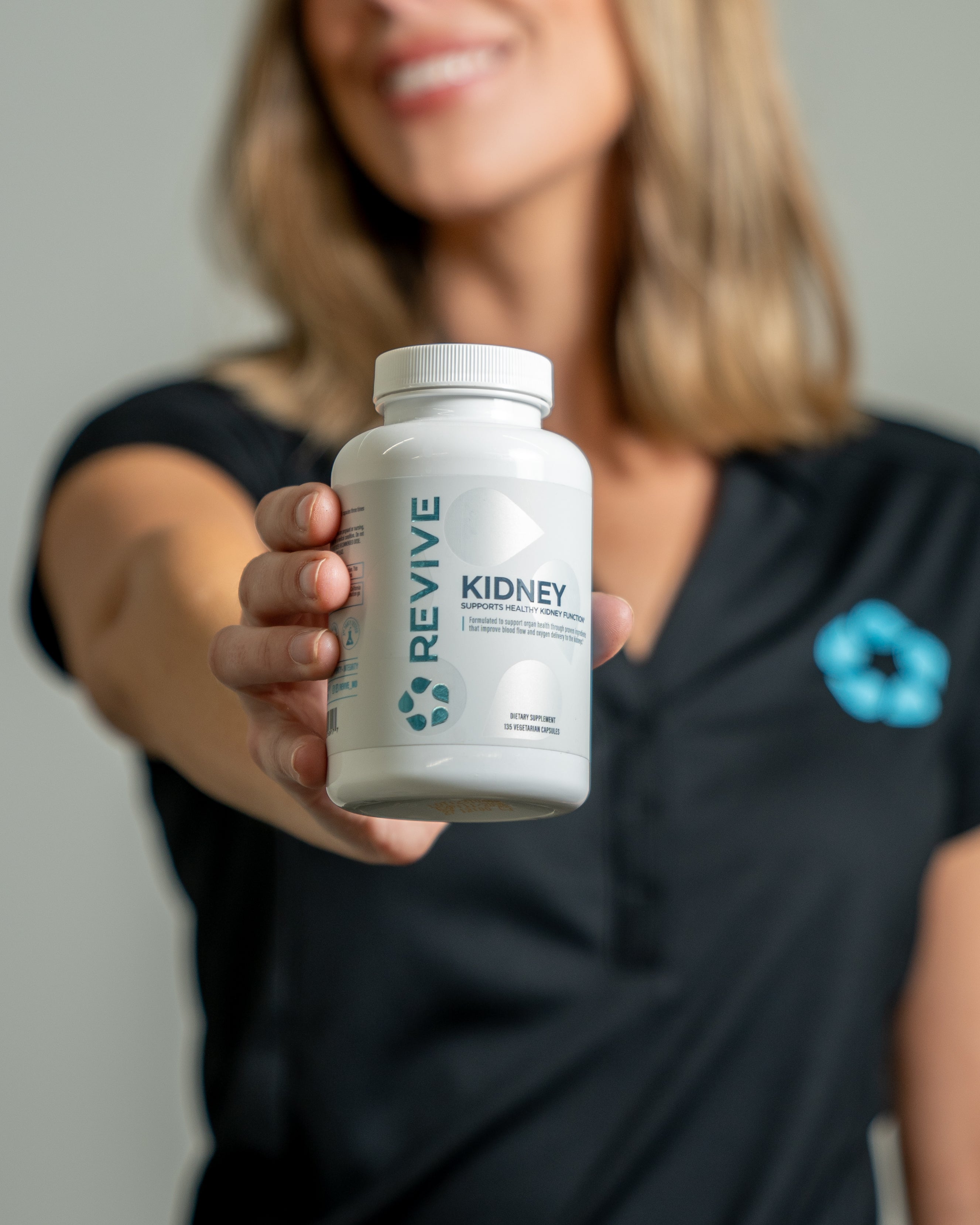 Person holding a bottle of Revive Kidney dietary supplement, formulated to support healthy kidney function and detoxification. Label features 180 vegetarian capsules.