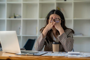 woman in glasses at work desk with hands on face looking stressed