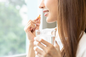 young woman smiling while taking a supplement pill and holding a glass of water