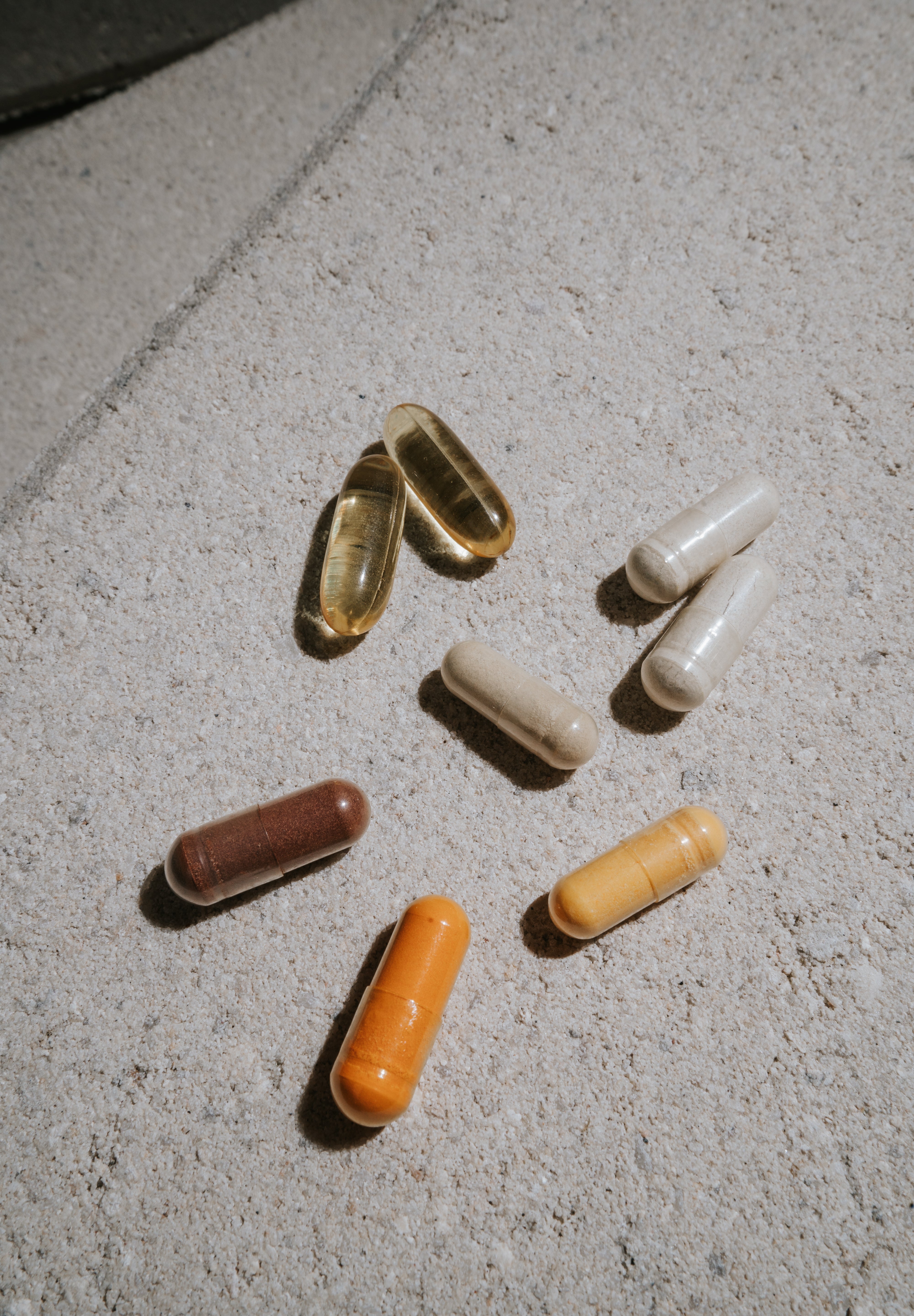 Flat lay of assorted multicolored capsules and softgel supplements arranged on a textured light gray stone surface